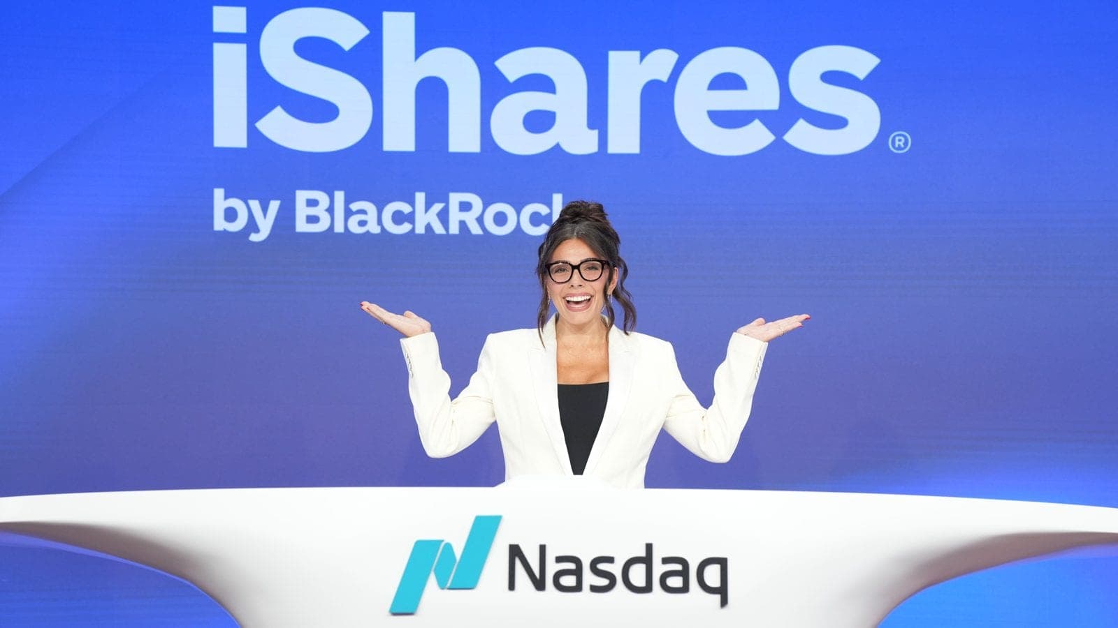 Taylor Price on the Nasdaq MarketSite balcony at the closing bell ceremony for the BlackRock iShares IQQ ETF launch, with the IQQ logo on the screen.